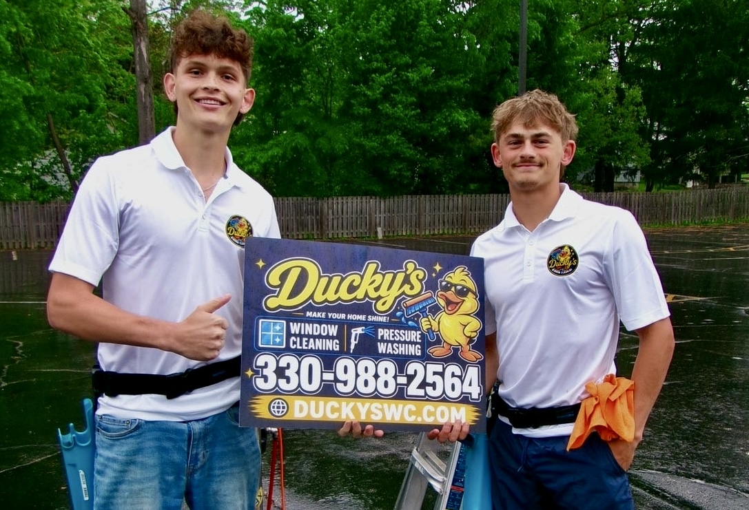 Beau and Hunter standing together holding a Ducky's yard sign